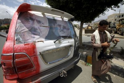 A man with carrying a weapon walks past a car adorned with a poster of Yemen's former President Ali Abdullah Saleh in Yemen's capital Sanaa